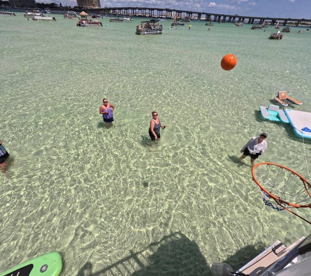 A beach with clear water, a basketball hoop, and people playing. 2