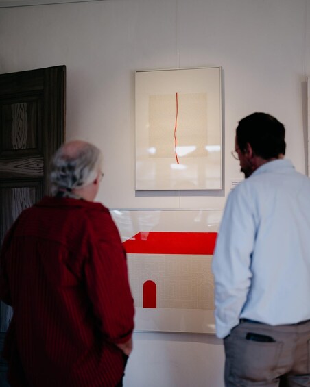 Two people observing an artwork with a red line on a white background. 3