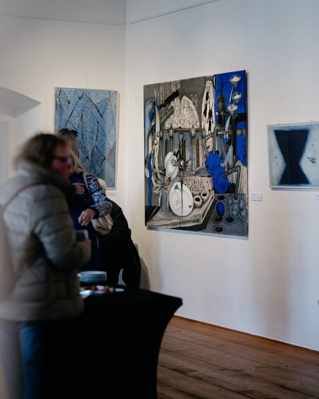 An art gallery with abstract paintings on the walls and a few people observing the art. 1