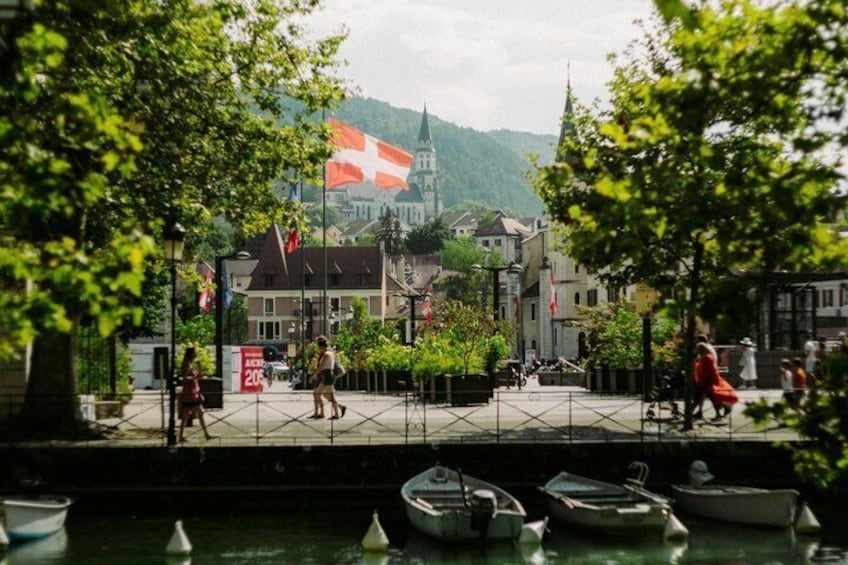 Un paseo fluvial con barcos amarrados, una iglesia con una bandera suiza y peatones. 1