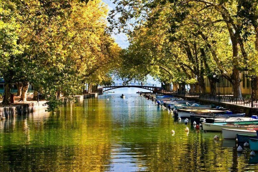 Un río tranquilo con barcas amarradas a la derecha, un puente a lo lejos y árboles bordeando las orillas. 5