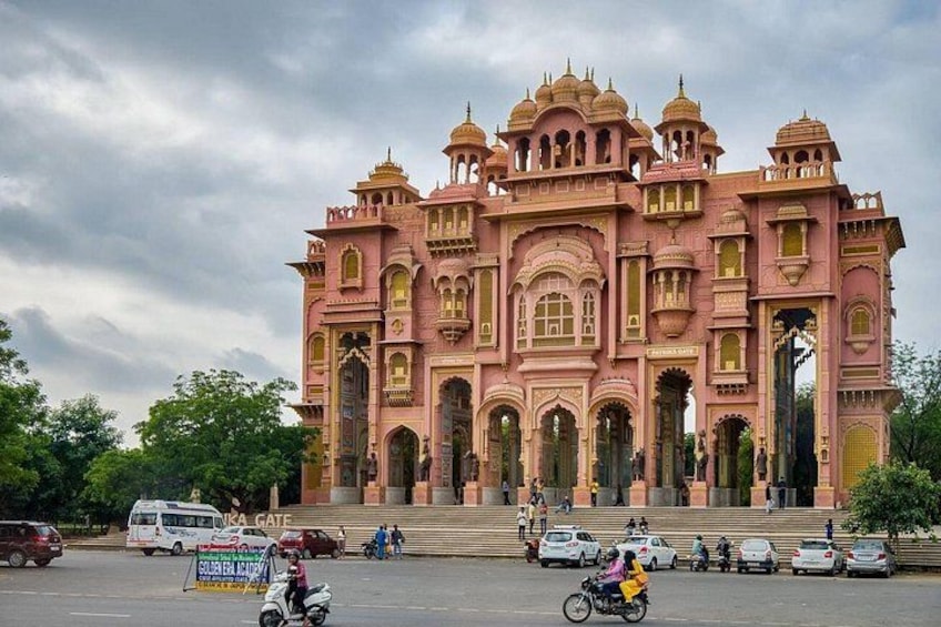 A pink palace with domes and arches, surrounded by trees and vehicles. 4