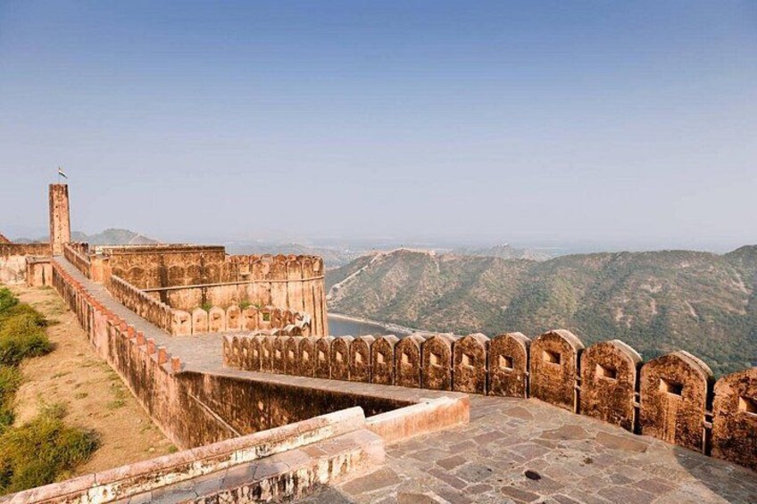 A historic fort with a watchtower, a stone wall, and a mountainous backdrop. 3