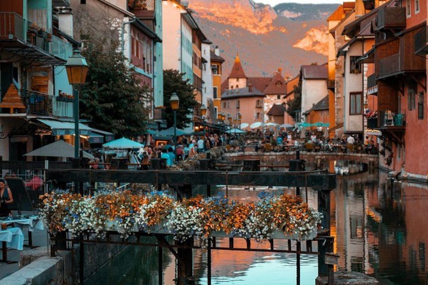 A riverside town with buildings, a wooden bridge, and flower arrangements. 1