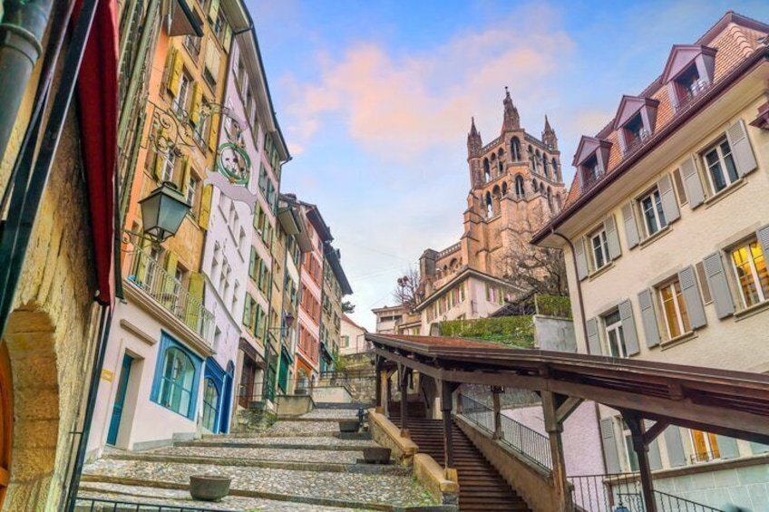 A narrow street with colorful buildings, a stone staircase, and a church in the background. 1