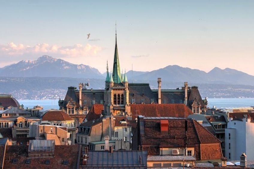 A cityscape with a prominent church spire, buildings with red roofs, and a mountain range in the background. 3