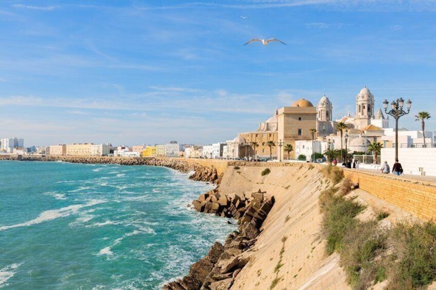Paesaggio costiero con spiaggia sabbiosa, costa rocciosa ed edifici storici con cupole e torri. 1