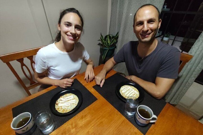 Zwei Personen sitzen an einem Holztisch mit Tellern voller Essen und Getränken. 3