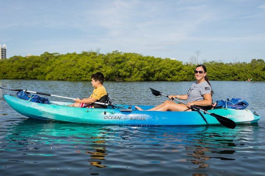 Two people kayaking on a calm body of water with a forested shoreline in the background. 3