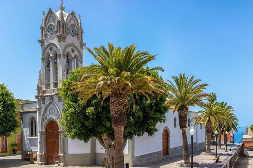 A white church with a bell tower, palm trees, and a clear blue sky. 1