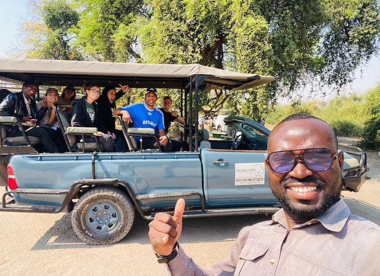 A group of people in a safari vehicle with a man giving a thumbs-up. 2