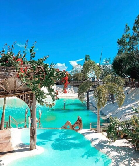 A clear blue pool with a person relaxing, surrounded by palm trees and a wooden pergola. 1