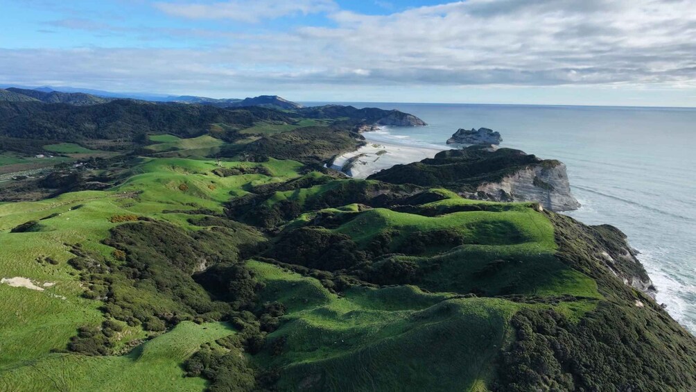 A coastal landscape with green hills, a winding road, and cliffs overlooking the sea. 4
