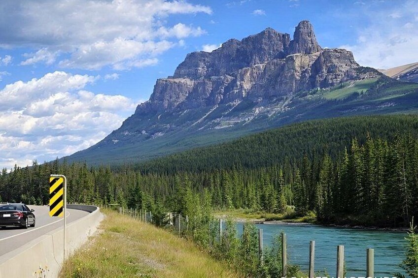 A mountain road with a guardrail, a car, a river, and a forested area. 2