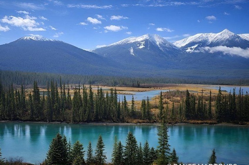 A mountain range with snow-capped peaks, a forested area, and a turquoise lake. 3