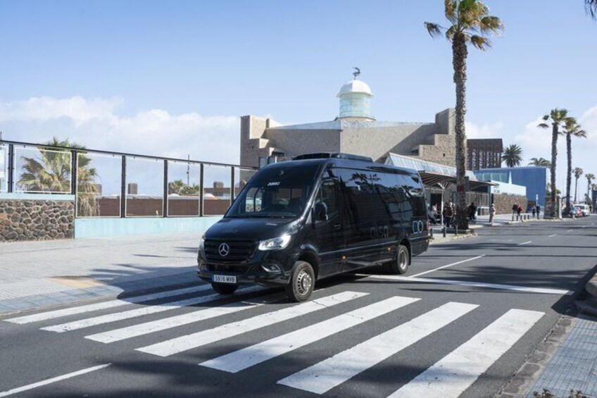 A black van parked on a crosswalk with palm trees and a building with a dome in the background. 1