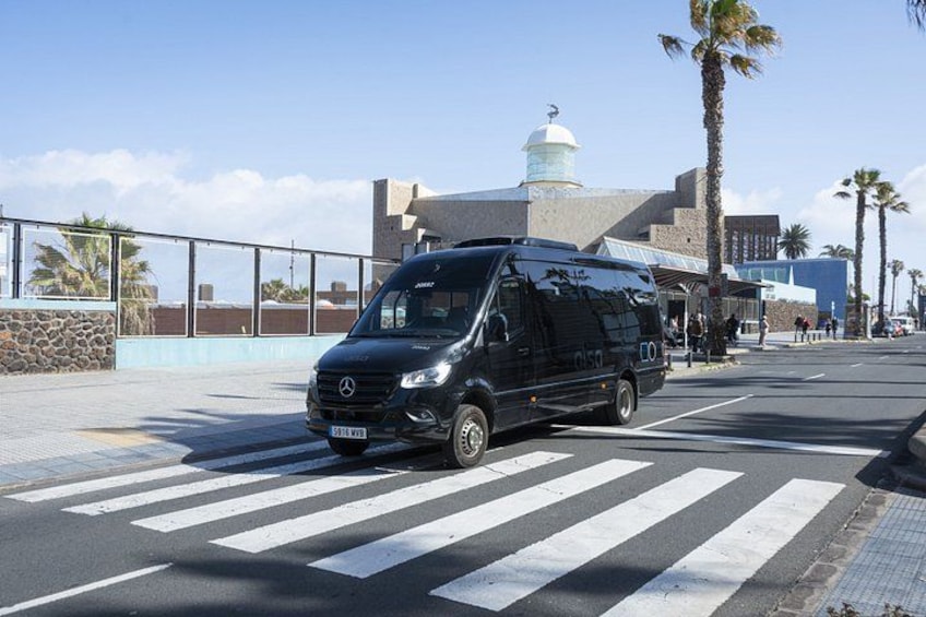 A black van parked at a crosswalk with palm trees and a building with a dome in the background. 1