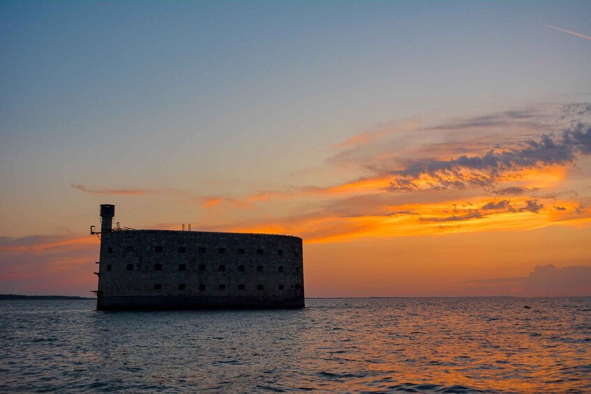 A large, cylindrical concrete structure in the water during sunset. 1