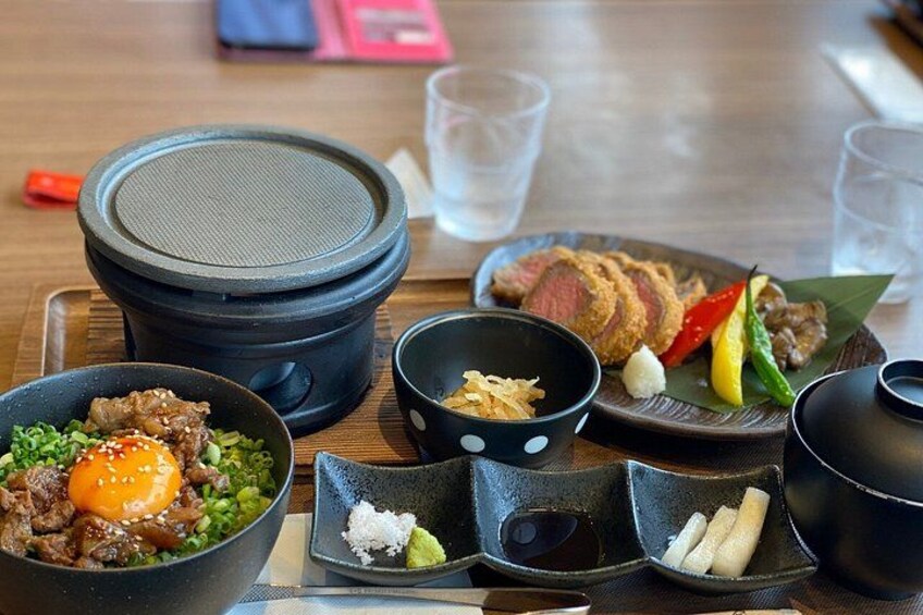 Ett urval av japanska rätter, inklusive en skål med nötkött och ägg, en tallrik med skivat nötkött och flera mindre rätter med tillbehör. 2