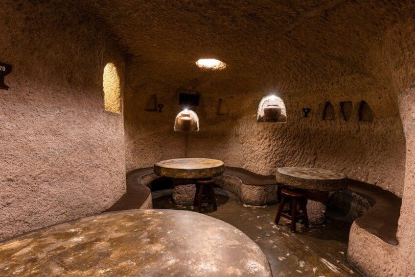 A cave interior with stone tables, benches, and a large stone slab. 3