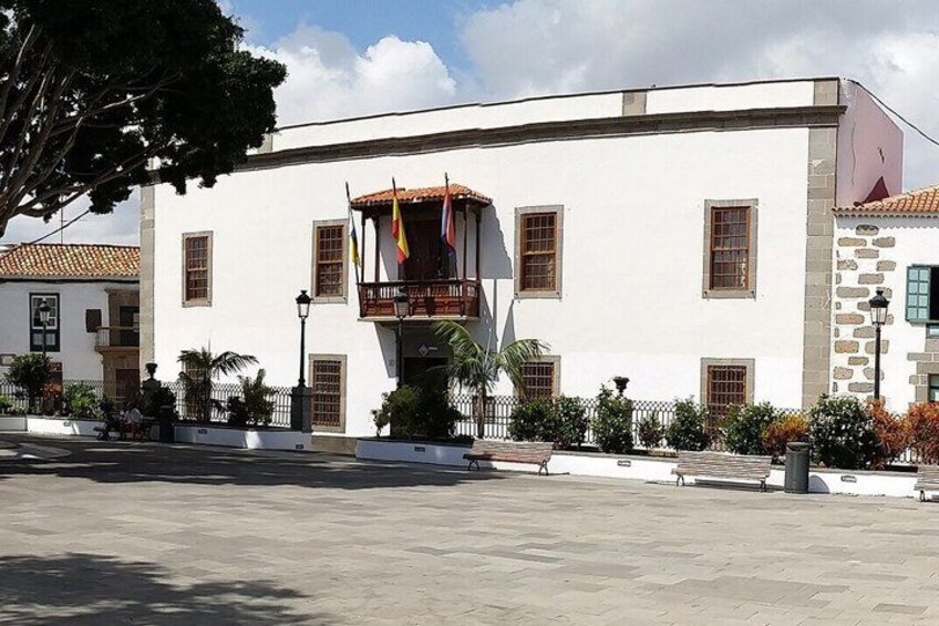 A white building with a balcony, flags, and a tiled roof. 2