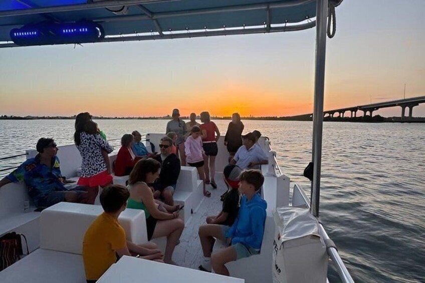 A group of people on a boat at sunset with a bridge in the background. 5