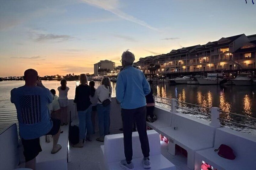 A group of people on a boat at sunset, overlooking a waterfront with buildings and boats. 4