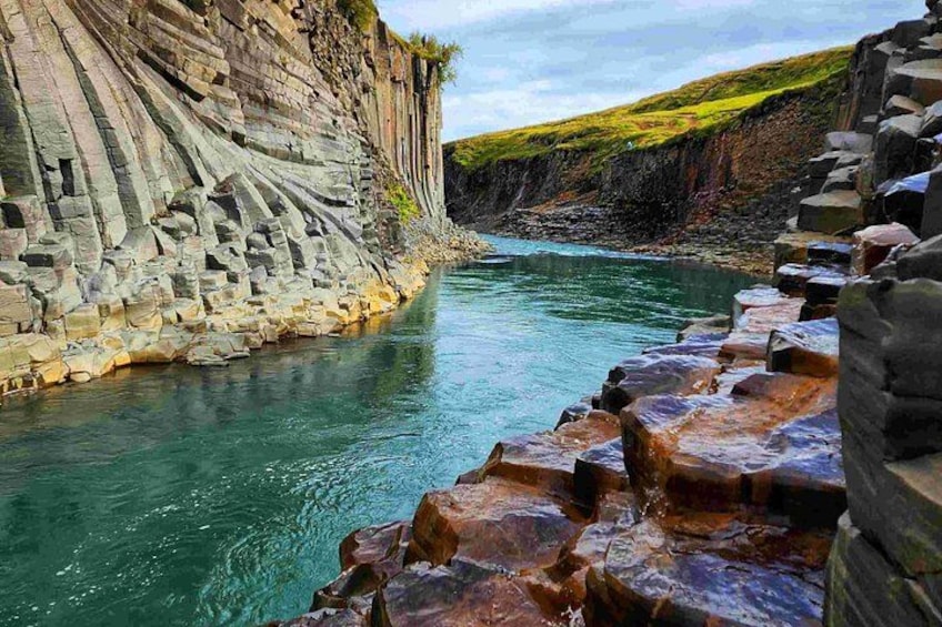 A coastal landscape with a river, rocky cliffs, and a series of large boulders. 1