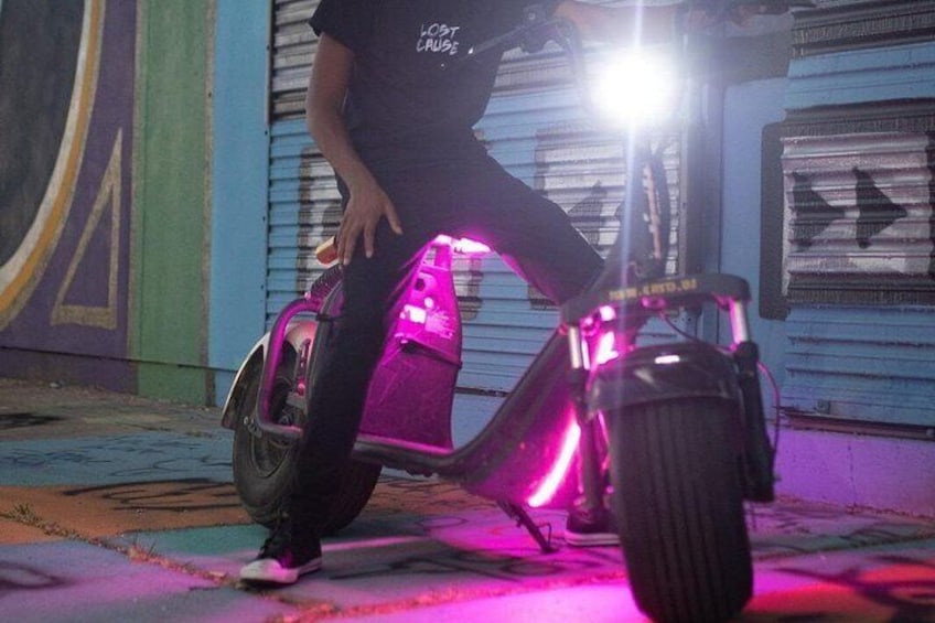 A person riding a brightly lit electric scooter on a street. 3