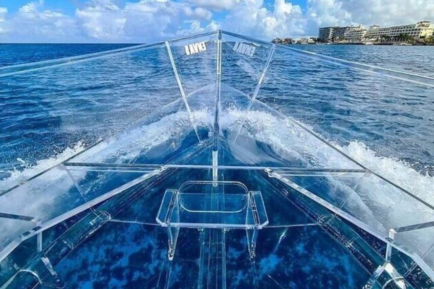 La prua di una barca solca acque blu calme sotto un cielo sereno, con edifici in lontananza sulla costa. 2
