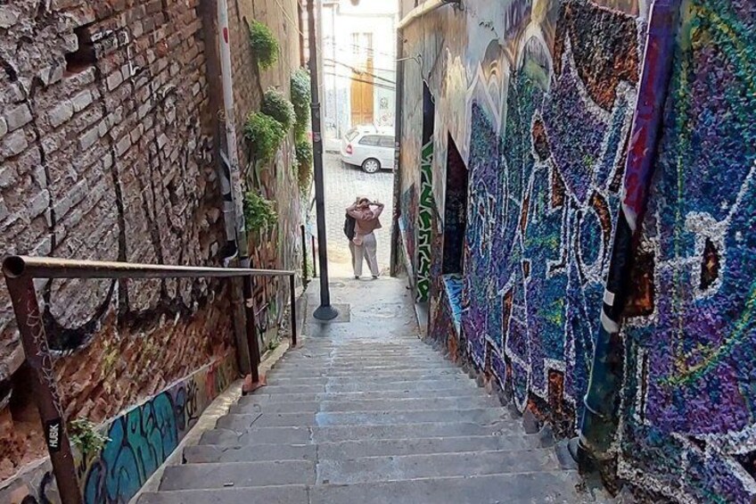 A narrow alley with graffiti-covered walls, a metal railing, and a person walking away from the camera. 3