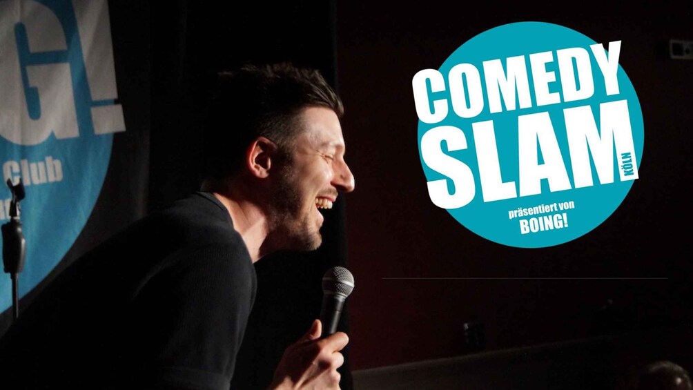 A person holding a microphone, likely performing or speaking, with a 'COMEDY SLAM' logo in the background. 4
