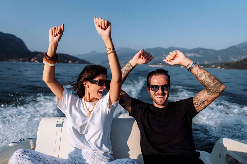 Two people on a boat with raised arms, water splashing behind them, and mountains in the background. 1