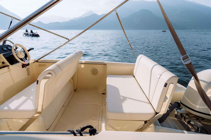 A boat interior with beige seats and a steering wheel, set against a backdrop of calm water and distant mountains. 5