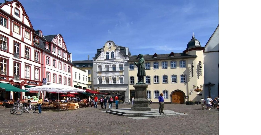A cobblestone square with historic buildings, a statue, and outdoor seating. 1