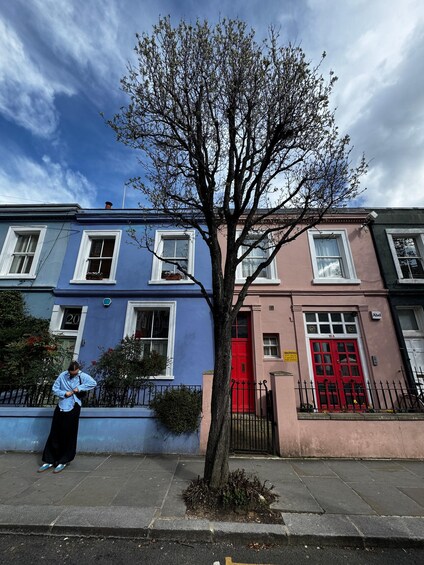 A tree in front of a row of houses with a person standing on the sidewalk. 3