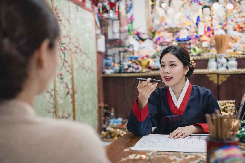 A person in traditional attire sitting at a table with a pen and paper, surrounded by various items and decorations. 1