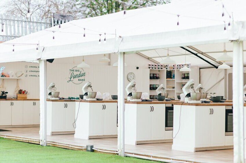 Een reeks witte keukens met bakbenodigdheden, onder een witte luifel, aangeduid met 'The Big London Bake'. 1
