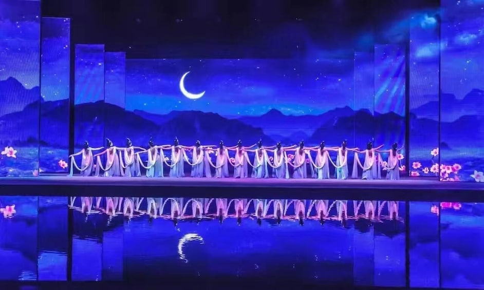 A stage with performers in pink costumes, a crescent moon, and a starry night sky backdrop. 5