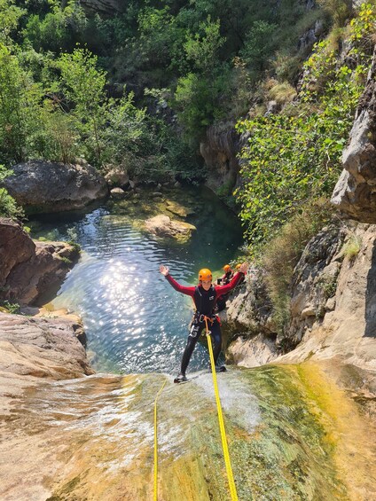 A person rappelling down a rocky cliff into a clear water body surrounded by greenery. 2