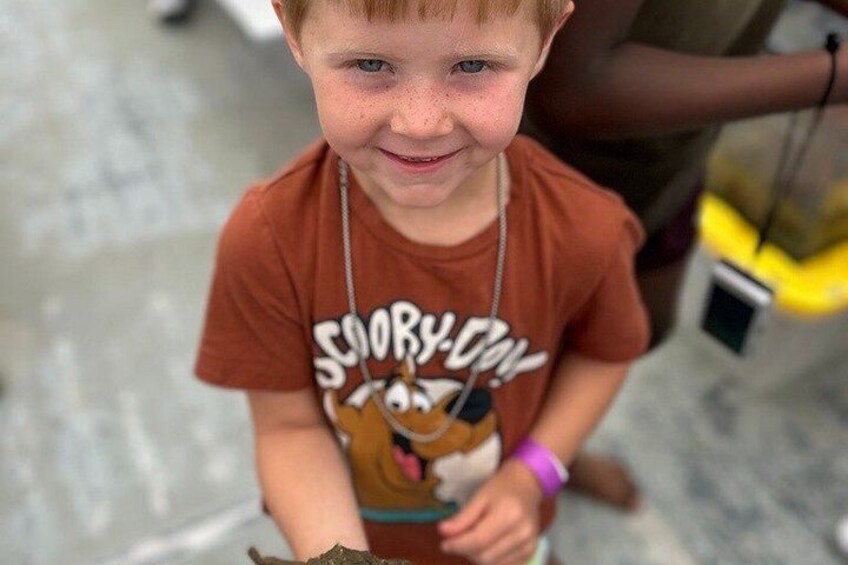 A child wearing a brown t-shirt with a cartoon character and text, holding a brown object. 3
