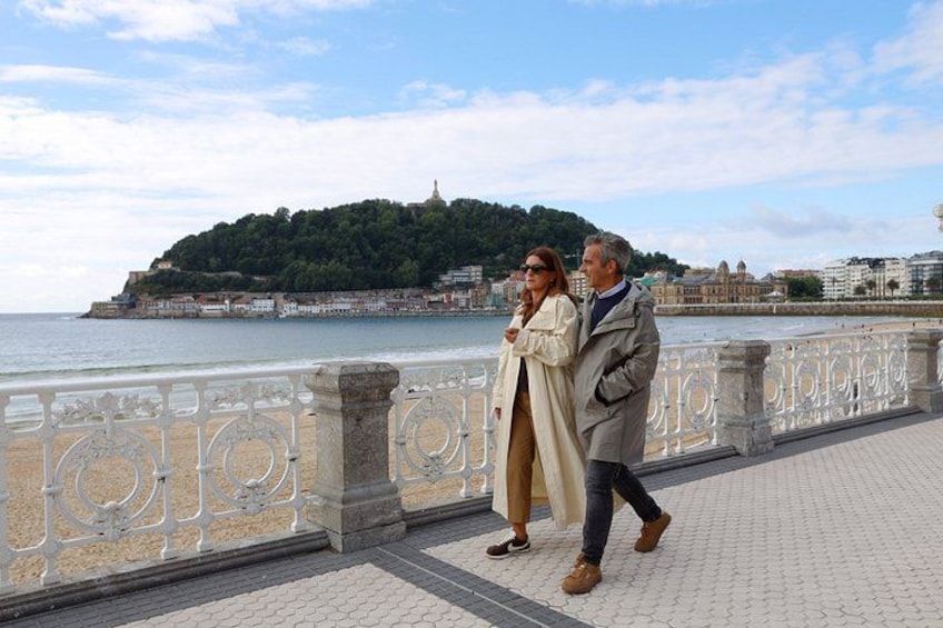 A coastal promenade with a stone railing, a distant hill with buildings, and a clear sky. 1
