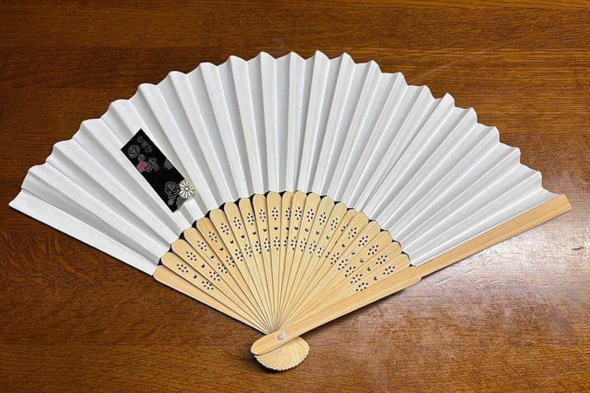 A white fan with a wooden handle and a black label on the back. 3