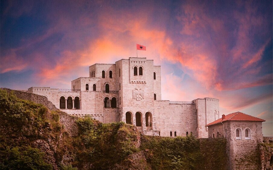 A historic stone fortress with a flag, arched windows, and a red-roofed tower. 4