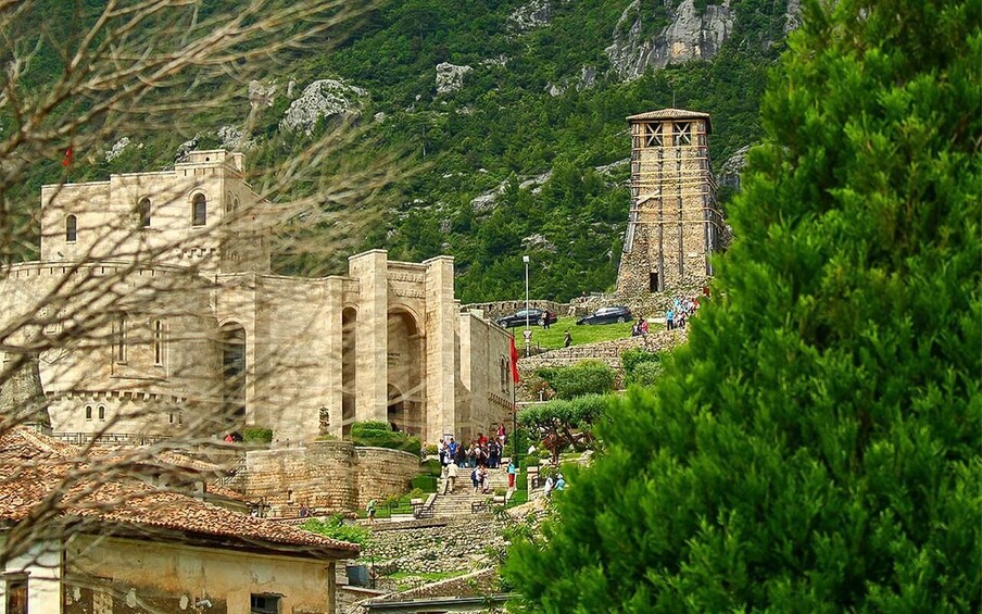 A historic stone building with a tower, surrounded by lush greenery and rocky terrain. 1