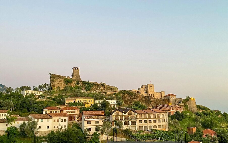 A historic fortified hilltop with buildings, including a prominent tower, overlooking a town with terraced houses. 2
