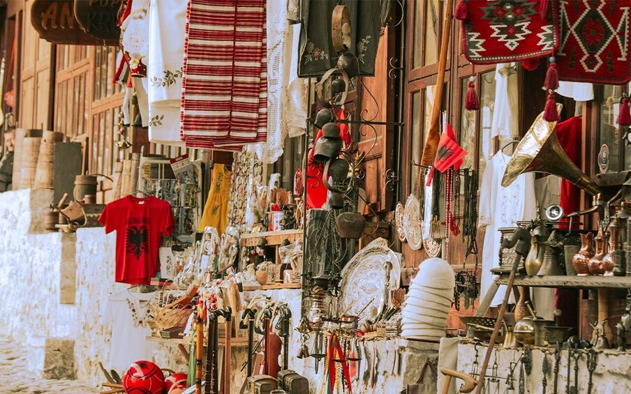 A narrow street with various shops displaying items like clothing, pottery, and metalware. 5