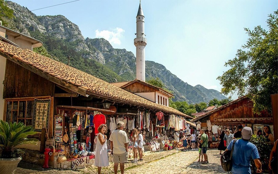 A bustling market street with shops, a mosque, and mountains in the background. 5
