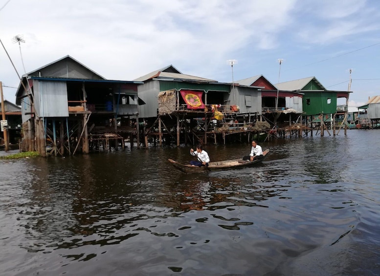A river with houses on stilts, a boat with two people, and a colorful banner. 5