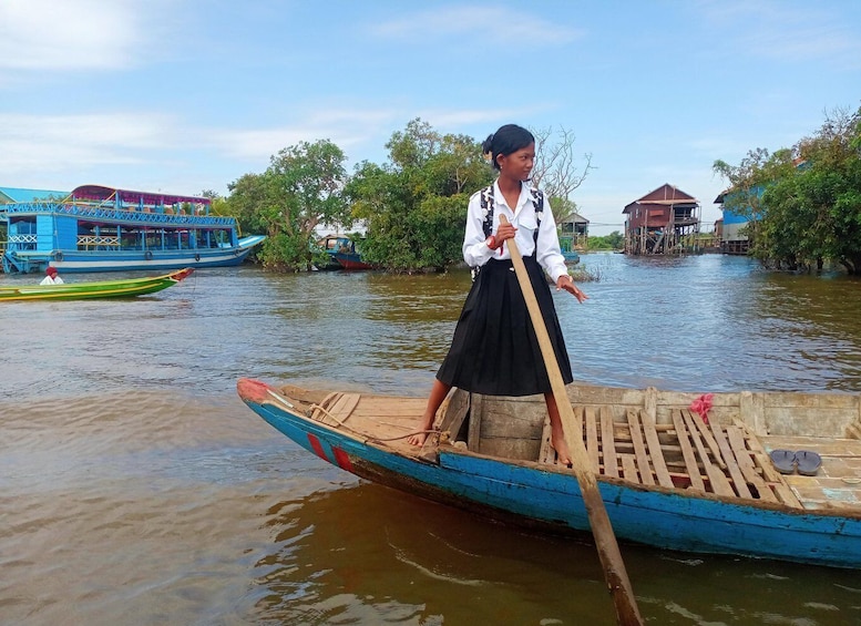 A person in a boat on a river with houses and boats in the background. 1